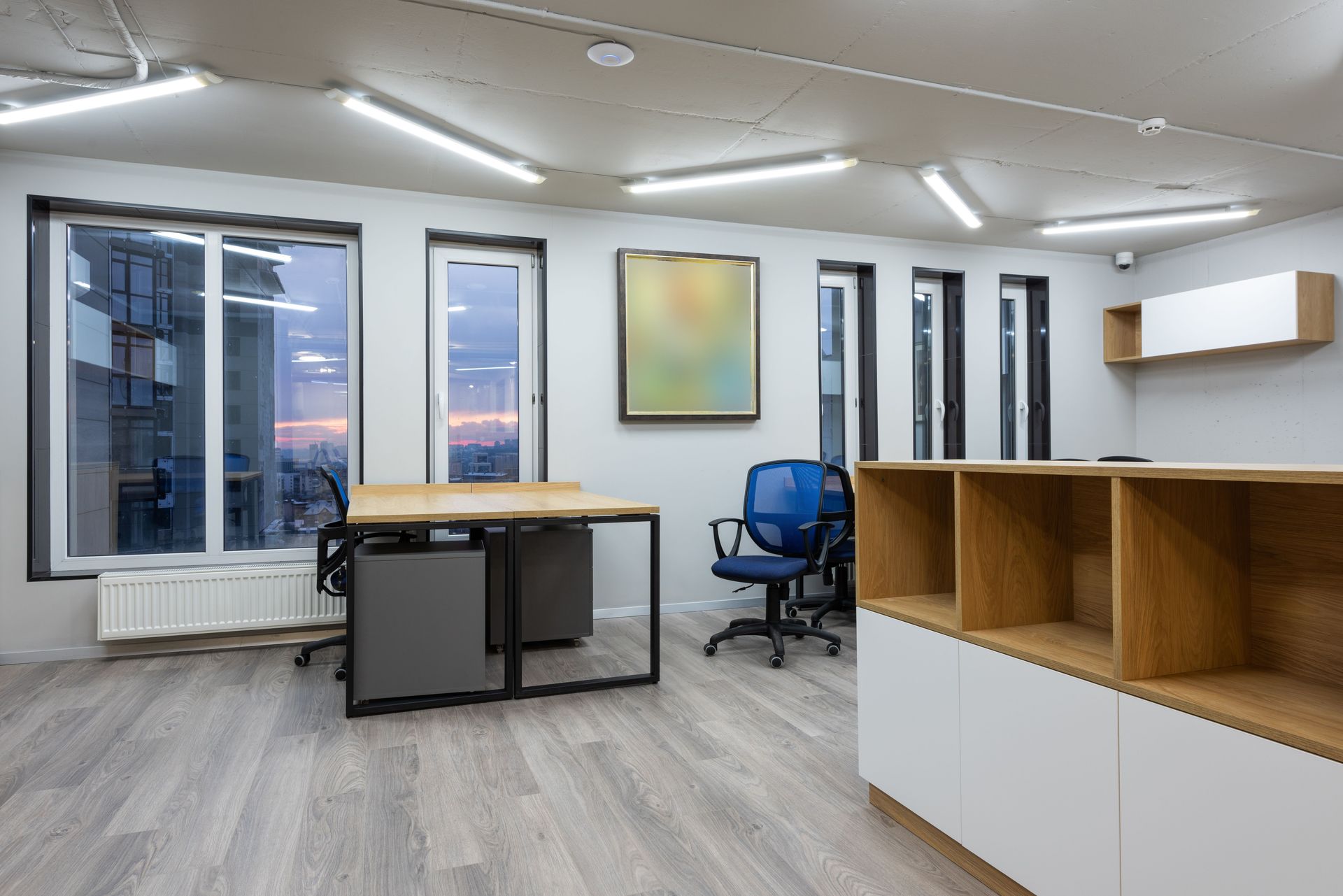 Interior of office with contemporary new wooden tables and chairs glowing by ceiling lamps